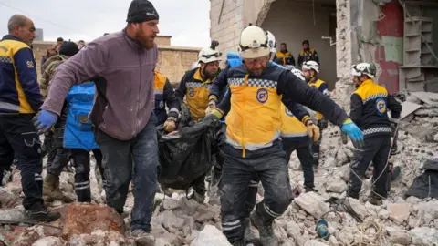 Rescuers carry a body bag across rubble