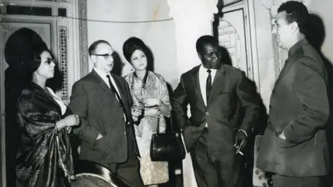 Yves Blouin-André, her husband, daughter, and principals chat in a group wearing elegant evening wear.