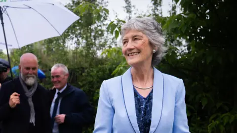 Catherine Connolly at the Chelsea Flower Show wearing a light blue jacket, with a darker blue top underneath. 