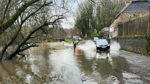 A car driving through flood water on a rural road.