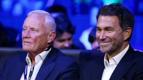 Getty Images Barry and Eddie Hearn sitting ringside at a boxing event. They are both smartly dressed in suits.