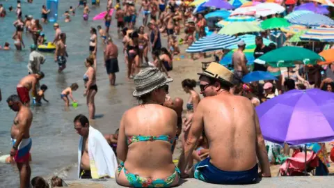 Getty Images A couple sit face to face opposite a Benidorm beach which is thronged with sunseekers, some of whom are sheltering from the blazing heat beneath coloured umbrellas