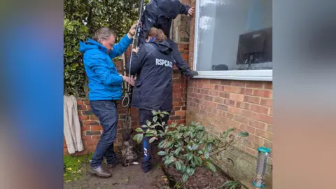 RSPCA Three people stood outside a house with a long metal rod after rescuing a cat from a tiny gap 