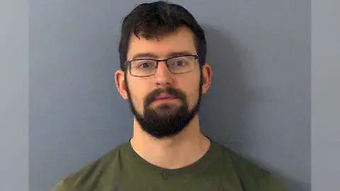 Thames Valley Police Benjamin Fields wearing a green top and glasses in a mugshot photo. He has dark hair and a thick dark beard.