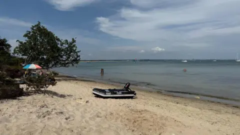 A sunny scene on a beach - a rib with a motor can be seen on the sand and people are in the sea