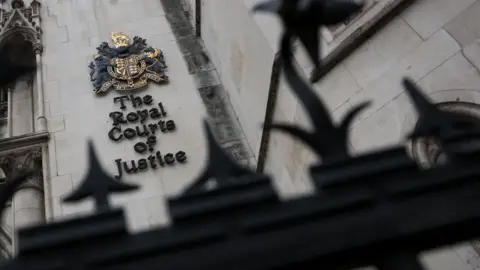 Reuters The Royal Courts of Justice: the words "The Royal Courts of Justice" written in black on a grey wall. The blurred top of a black fence can be seen in the foreground.