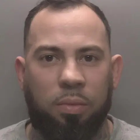 Leicestershire Police A man with dark hair and a beard and brown eyes, wearing a grey top