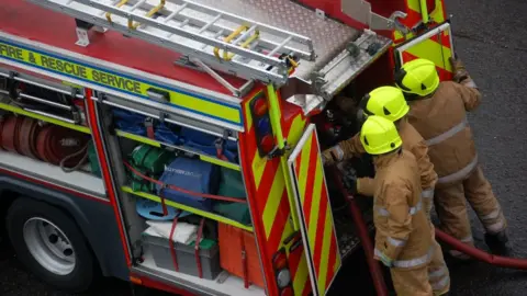 Three firefighters at the back of a fire engine. 