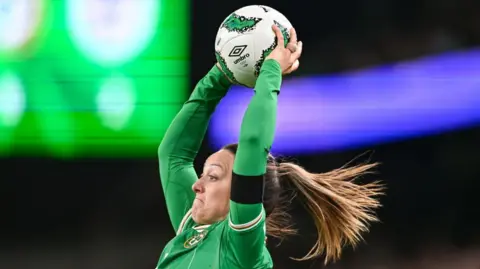 Getty Images Megan mid throw in. She is in a green Republic of Ireland jersey and has blond highlights in her ponytail. Her face is concentrated and the ball is above her head.