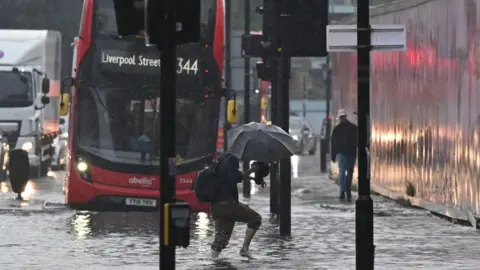 Getty Images man walking through floods with bus in background