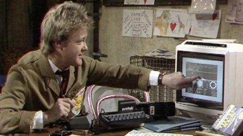 Keith Chegwin sits at his computer and points at the screen