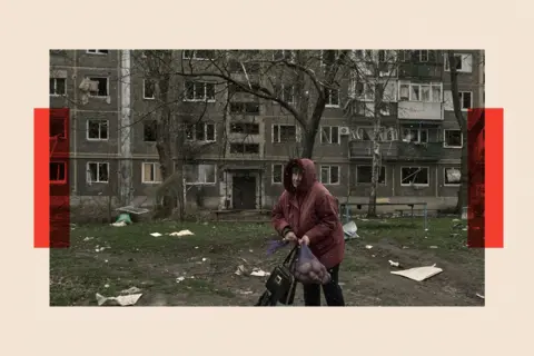 Libkos/Getty Images A woman carries a sack of potatoes by damaged residential buildings in Pokrovsk, Ukraine
