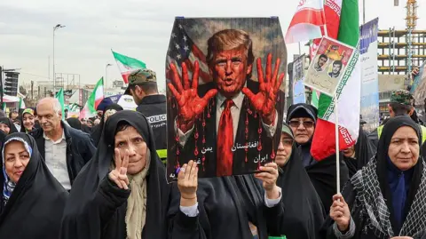 AFP via Getty Images Supporters of the Iranian regime demonstrate against President Trump in 2026. They are holding up a poster showing the US President with bloodied hands