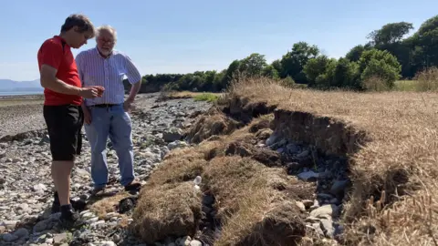 Dale Spridgeon Two men examine the coastal erosion of the land as it meets the beach