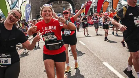 Lauren Jean Lauren Jean, wearing a red t-shirt with her name and a heart logo on the front, gives a thumbs up while jogging in a crowd of marathon runners