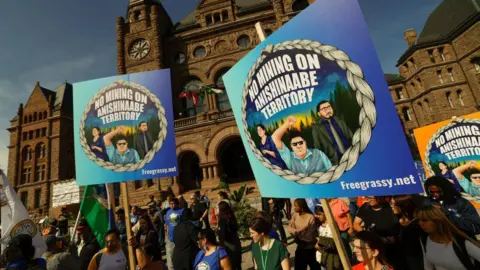 Protest signs read: No mining on Anishinaabe Territory while a crowd gathers outside Queens Park, Ontario's brick-clad provincial legislature