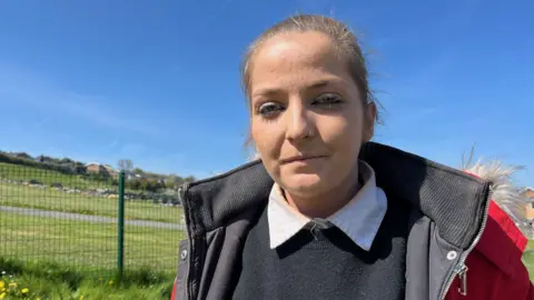 Lauren Jones, stood at the forefront of Holywell cemetery and looking at the camera. She has her hair tied back and wears a red jacket over a black sweatshirt.