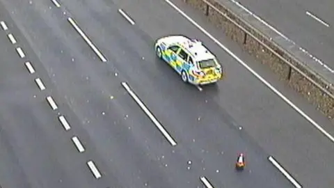 A police car on the A14, showing several lanes of the road empty and one traffic cone.