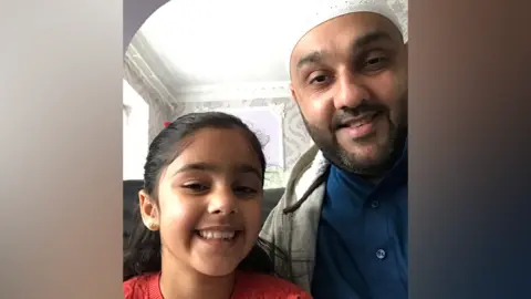 Imran Bahar and his daughter Zaira pose for a selfie. They are both smiling at the camera.