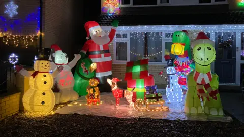 A snowman, dinosaurs, Santa and a snowman figures illuminated by lights.