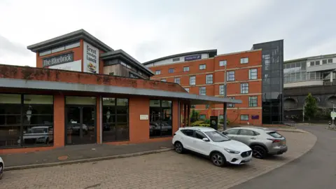 A red brick restaurant building in front of a five-storey red brick building with a Premier Inn signs on the building 