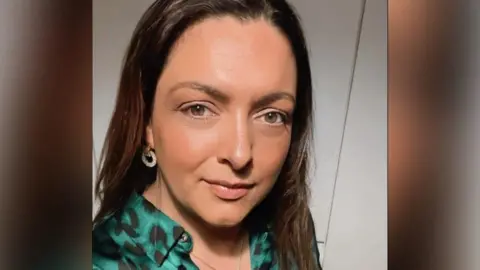 Kerry Anne Hartnett A photo of a woman wearing a green leopard print shirt with long brown hair, smiling at the camera.