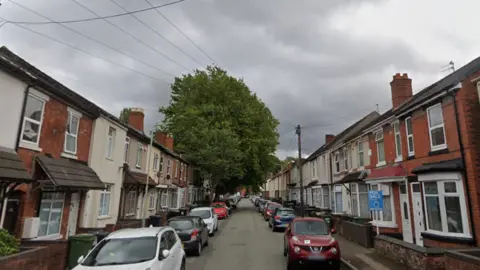A view of a narrow street of terraced houses in Wolverhampton, with cars parked along both sides.