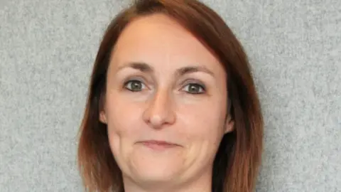 ICB A lady with shoulder-length brown hair is smiling at the camera in a close-up photo.