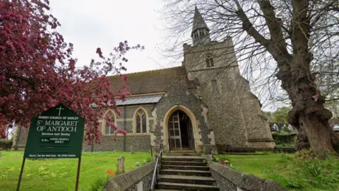 Google Steps leading up to the entrance of a church which has a sign in the foreground saying: "Parish church of Barley" and "St Margaret of Antioch". There are trees on the left and right of the picture with grass either side of the steps with some tombstones.