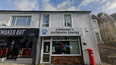 Google The exterior of Bridgend Adult Resource Centre. The building is painted white. It has a logo that resembles a paw print. In front of the right had side of the building is a red post box 