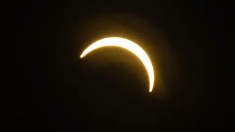 BBC / Jack Valpy A bright crescent of sunlight appears against a black sky as the Moon passes in front of the Sun during a partial solar eclipse.