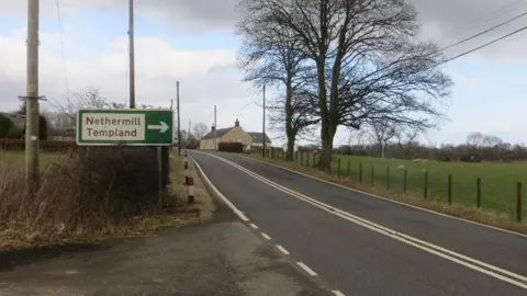 Richard Webb The A701 in Dumfries and Galloway with trees and a fence at the side and a sign for Nethermill and Templand