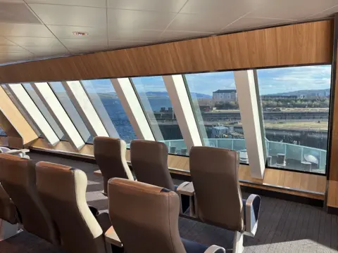 Brown vinyl covered seats face out of the angled windows at the front the ship in the forward observation area