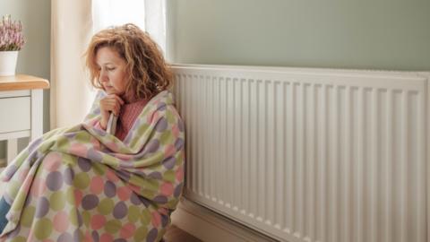 A woman in a blanket next to a radiator
