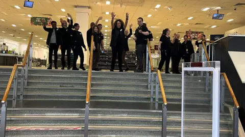 Employees wave as they close their store for the last time