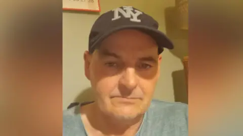 John Gretton has a black New York Yankees baseball hat and grey T-shirt