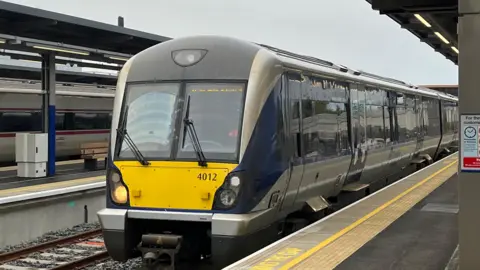 A translink train, painted yellow, blue and grey, stationary on the rail lines at Belfast's Grand Central Station