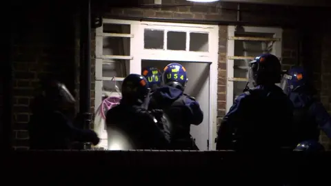 BBC Police officers enter property in protective gear