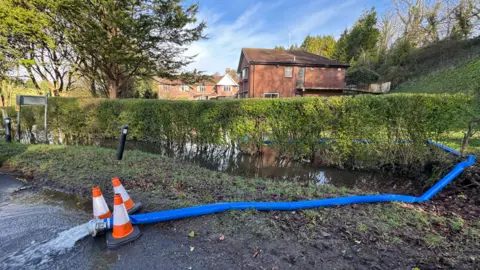 Outside Casterbridge Lodge on Saturday morning. Water is seen flowing from the pump hose close to the building. There are three orange and white cones around the hose.