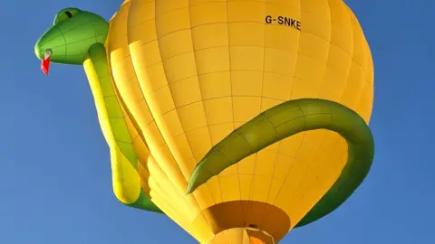 Adrian Connor A yellow hot air balloon, with a green 3D snake wrapped around it