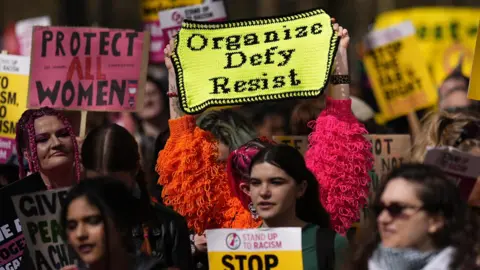 PA A group of women holding up signs at a rally. one of the signs his crocheted and reads organise, defy, resist.