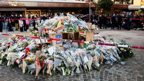AFP via Getty Images Flowers and candles laid in tribute to victims are displayed at a makeshift memorial following the fire at Le Constellation bar.