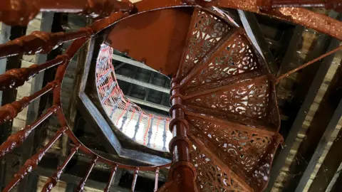 Jodie Halford/BBC A spiral staircase made of intricate cast iron patterns leads to a loft space filled with light.