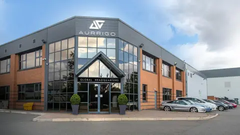 Aurrigo A new modern office building with glass frontage and several cars parked outside. Aurrigo is written on the building.