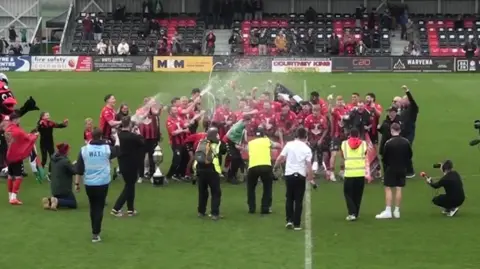Truro City Football Club players on the pitch at Truro Community Stadium. The players are celebrating after the win.