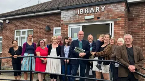 Group of people standing in front of the brick building of the library looking at the camera.