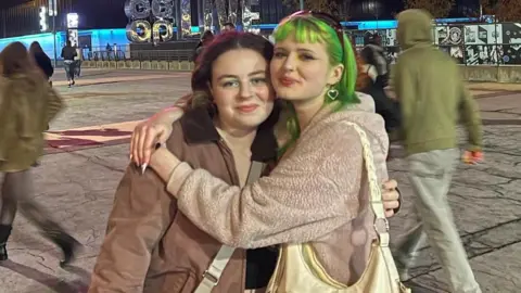 Freya and Niamh extracurricular  the Co-op Live Arena successful  Manchester. Niamh has dyed greenish  hairsbreadth  and has her arms astir   Freya, who nods to the Brat taxable   with greenish  oculus  shadow. They're some  wearing brownish  coats and grin  astatine  the camera. 