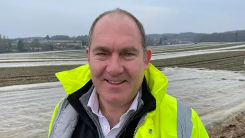 Jon is standing in a field and wearing a reflective jacket