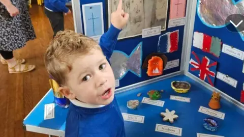 Supplied A little boy in a blue school jumper points at an art display.