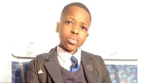 Family handout A boy sitting on a bus in school uniform, looking at the camera